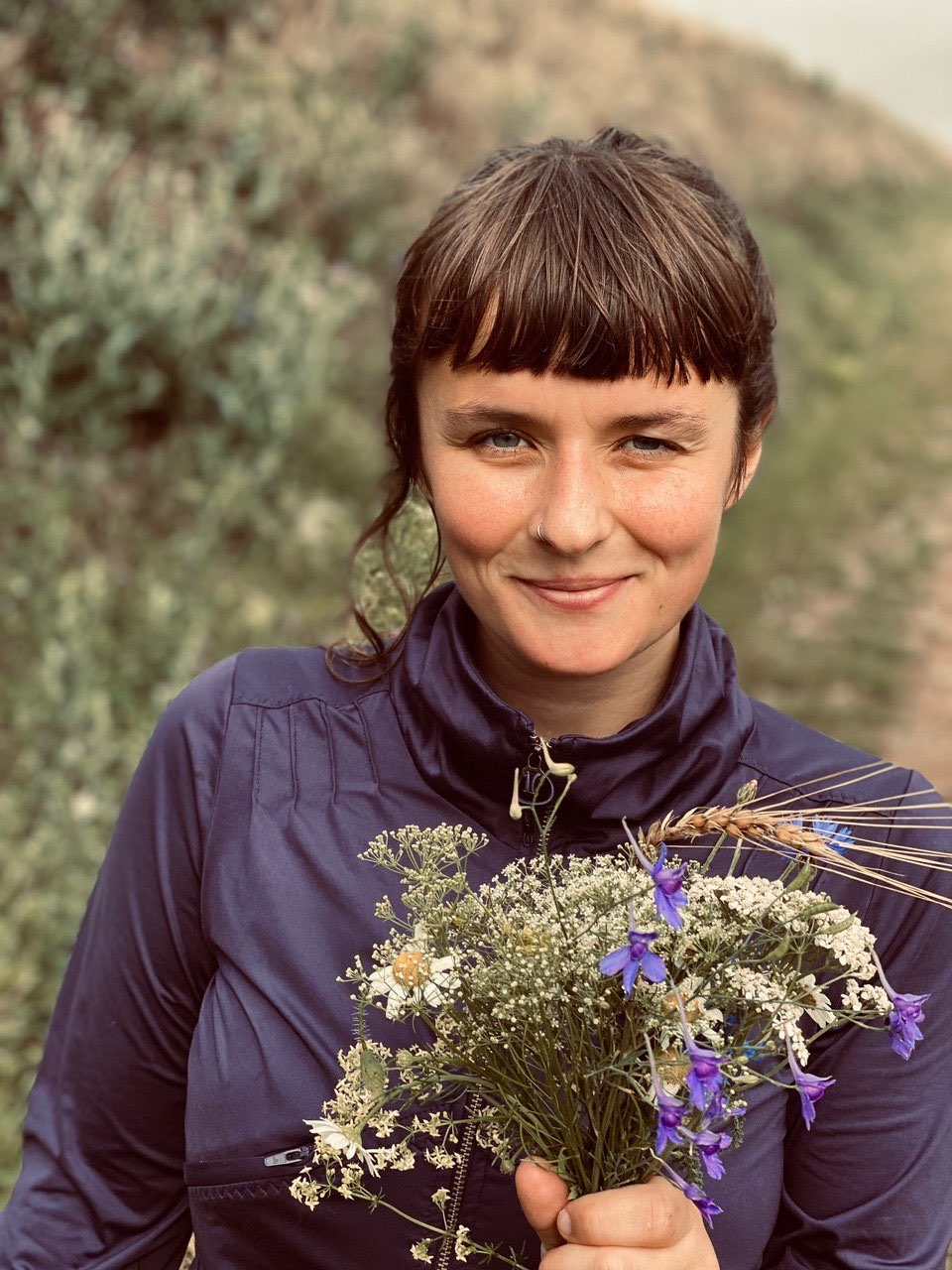 Portrait von Kollektivmitglied Judith in der Natur. Sie hält einen Blumenstrauß und lächelt in die Kamera.